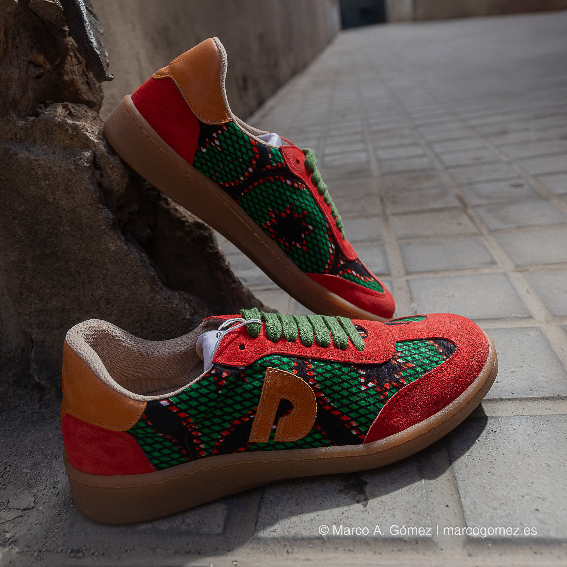 Proyecto integral Zapatillas con diseño en rojo y verde de la colección Dakart apoyadas sobre suelo adoquinado en exteriores.