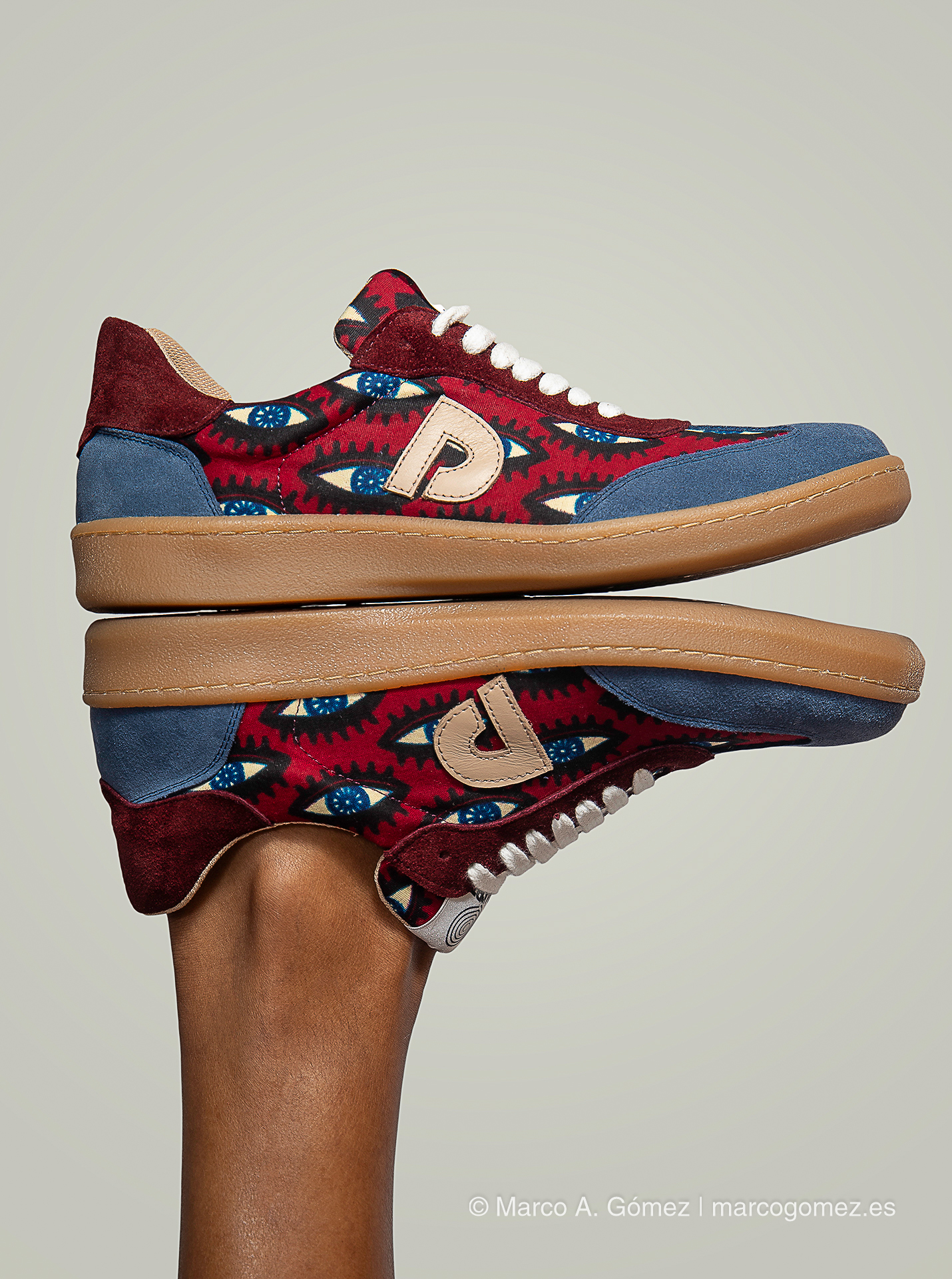 Proyecto integral Primer plano de zapatillas con estampado de ojos en tonos burdeos y azules junto a un fondo urbano de la marca Dakart.